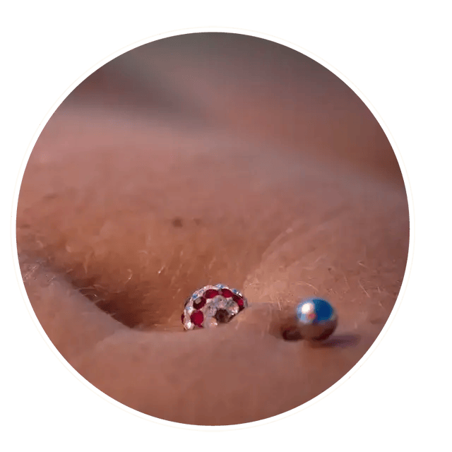 Close-up of a navel piercing with a red zirconia and titanium jewelry, ideal for body piercings.